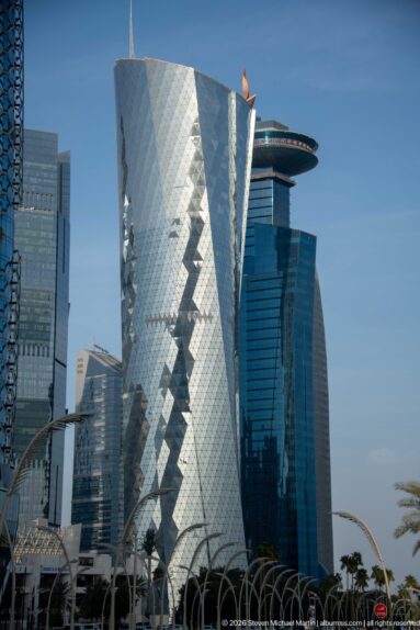 Angular silver-glass high-rise with faceted surfaces and a diagonal diamond-patterned façade among neighboring towers.