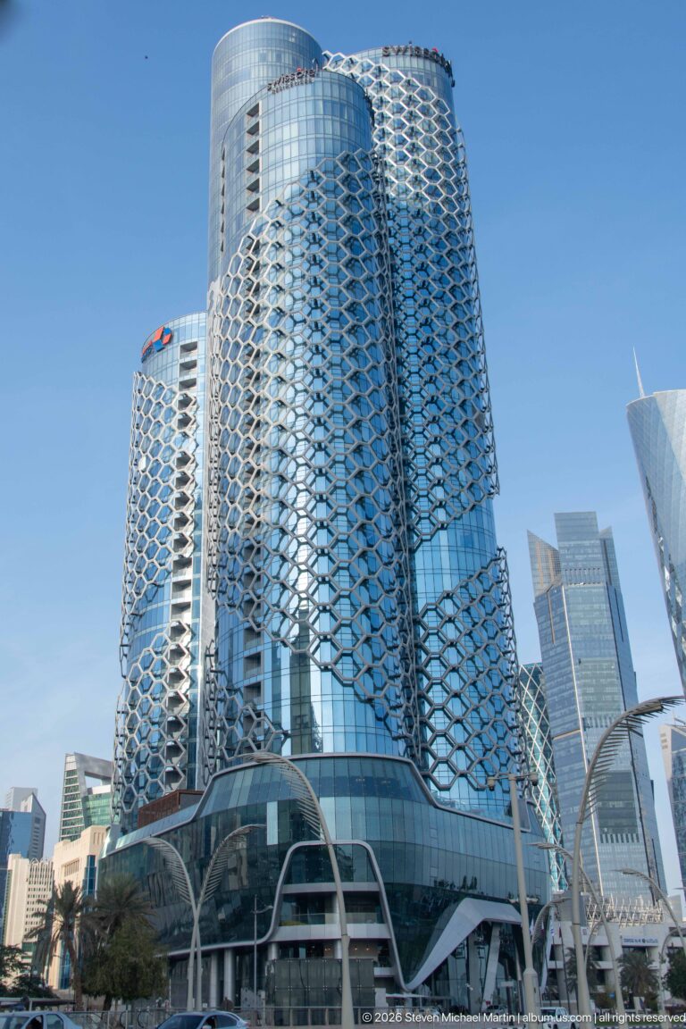 Two rounded glass towers wrapped in repeating silver geometric façade screens, with curved canopies at street level.