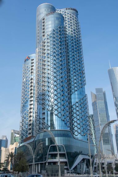 Two rounded glass towers wrapped in repeating silver geometric façade screens, with curved canopies at street level.