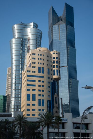 Cluster of pale stone and blue-glass high-rises with palm trees and curved streetlights in Doha.