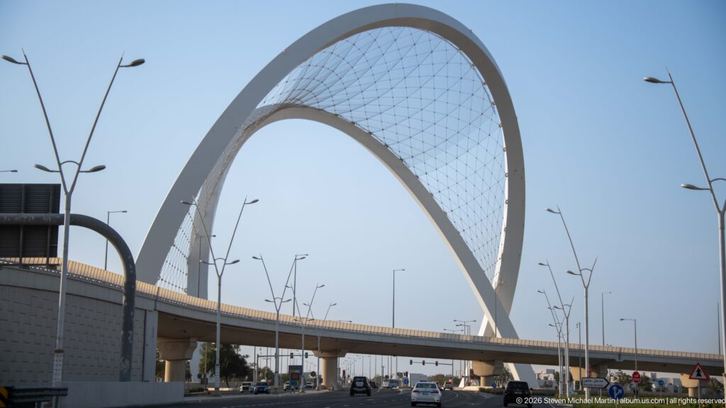 Large white network-arch bridge over a multilane road with cable webbing and modern streetlights.