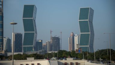 Two matching green-glass towers made of offset rectangular blocks with other high-rises and cranes behind.