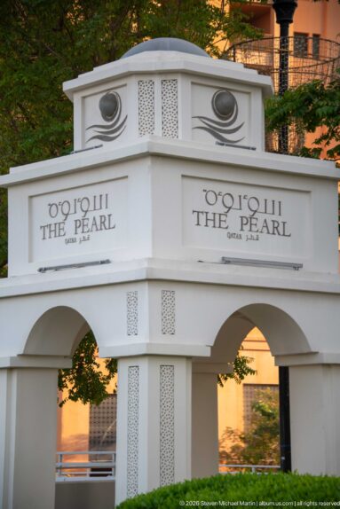 White arched gateway marked The Pearl Qatar in English and Arabic with decorative panels.