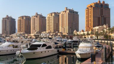 White motor yachts moored in a marina with tall cream and ochre residential towers behind at The Pearl-Qatar.