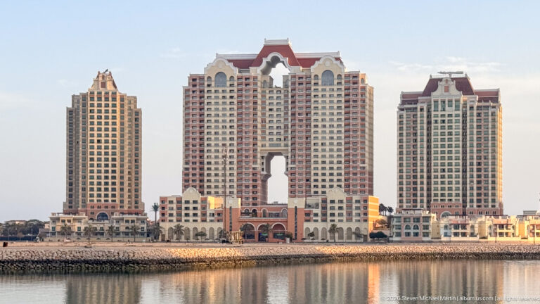 Three cream residential towers with red roofs and a large central arch beside the waterfront at The Pearl-Qatar.