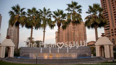Large The Pearl sign in English and Arabic with palms and high-rise residential towers behind.