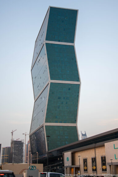 Green-glass high-rise made of three offset rectangular blocks above low commercial buildings.