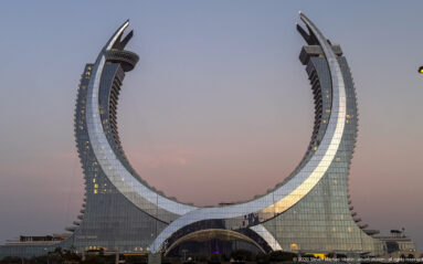 Katara Towers in Lusail, two curving glass towers forming a dramatic crescent-like silhouette at dusk.