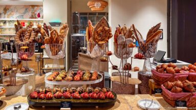 Hotel bakery buffet with croissants, pastries, baguettes, braided breads, and tall loaves arranged on tiered stands.