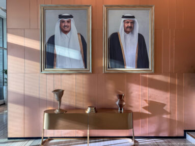 Two framed portraits of Qatari leaders above a console table with decorative metal vessels on a paneled wall.