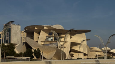 National Museum of Qatar with overlapping desert-rose-inspired discs and curving streetlights in warm late-day light.