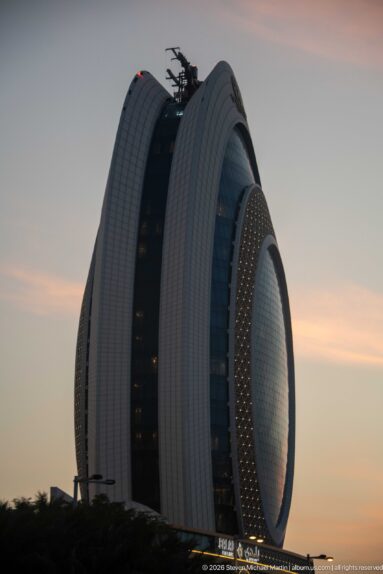Close view of a rounded glass tower wrapped in broad white ribs with a perforated oval screen.