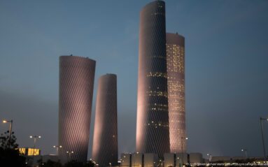 Four softly lit twisting Lusail Plaza Towers rise above low buildings at twilight.