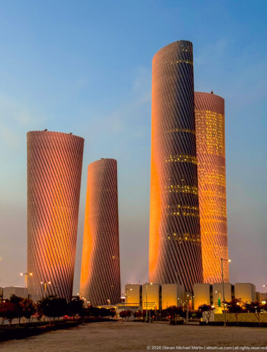 Four twisting Lusail Plaza Towers glow orange and pink against a clear dusk sky.