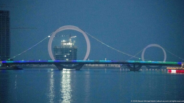 Illuminated bridge spans the water beneath two circular cable arches, framing a tower in the larger ring.