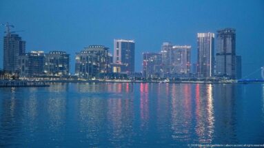 Modern Lusail waterfront towers reflect white and colored lights across calm evening water.