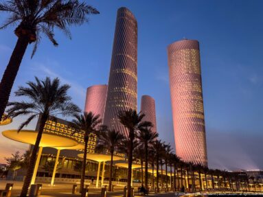 Pink and lavender Lusail Plaza Towers rise above palms and warmly lit podiums at blue hour.