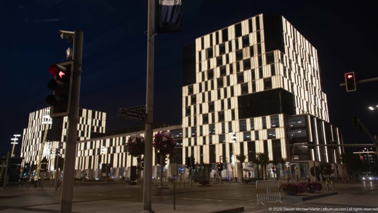 Modern illuminated blocks rise beyond traffic lights at a broad Lusail intersection at night.