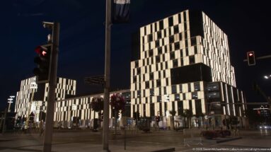 Modern illuminated blocks rise beyond traffic lights at a broad Lusail intersection at night.
