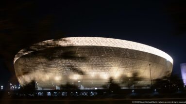 Night profile of Lusail Stadium with a bright rim and glowing perforated golden façade.