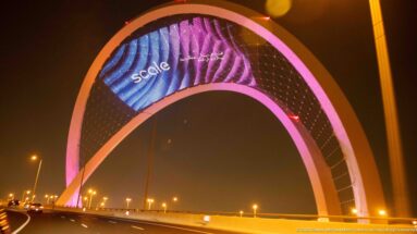Pink-lit 5/6 Arch spans a multi-lane roadway with a large animated digital display overhead.