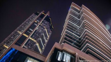 Low-angle night view between two modern high-rises with diagonal framing and bright horizontal edge lights.