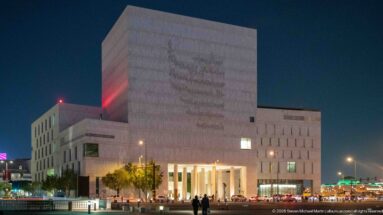 Large pale stone institutional building with a tall recessed colonnaded entrance illuminated at night.