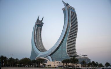 Katara Towers curve inward like a crescent above palms and low buildings at dusk.