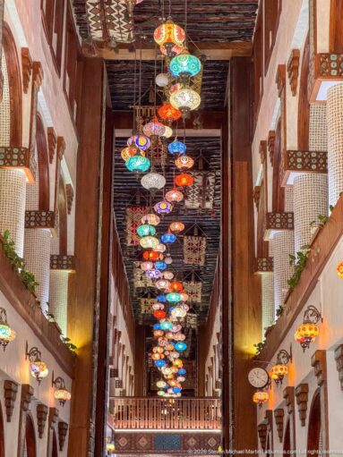 Long multi-level interior filled with rows of colorful hanging lanterns beneath timber beams.