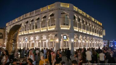 Large illuminated two-story arcaded building overlooks a crowded pedestrian plaza at night.