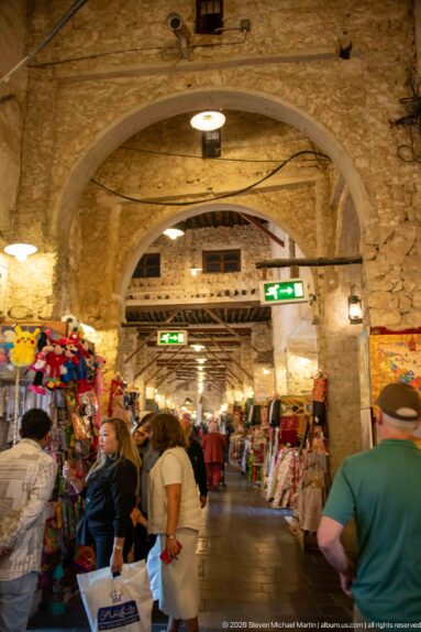 Shoppers walk through an arched stone market passage lined with colorful souvenir and textile stalls.