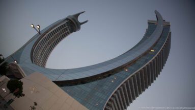 Katara Towers curve inward like a crescent, with glass façades and forked crowns rising above the podium.