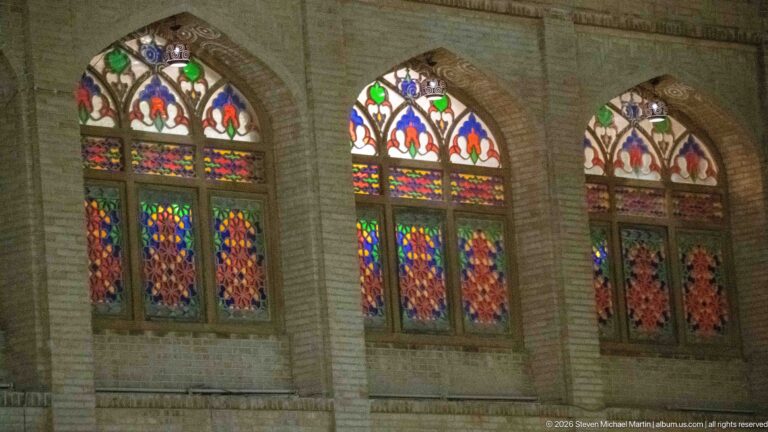 Three pointed-arch windows with colorful patterned glass repeat along a pale masonry façade at night.