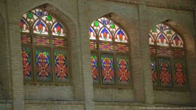 Three pointed-arch windows with colorful patterned glass repeat along a pale masonry façade at night.