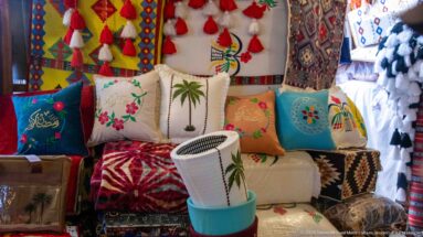 Colorful embroidered cushions, patterned textiles, tassels, and a woven basket densely displayed in a Souq Waqif stall.