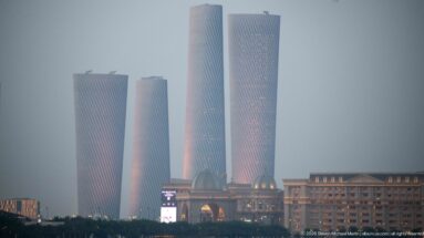 Four twisting Lusail Plaza Towers rise through haze above lower buildings in soft evening light.