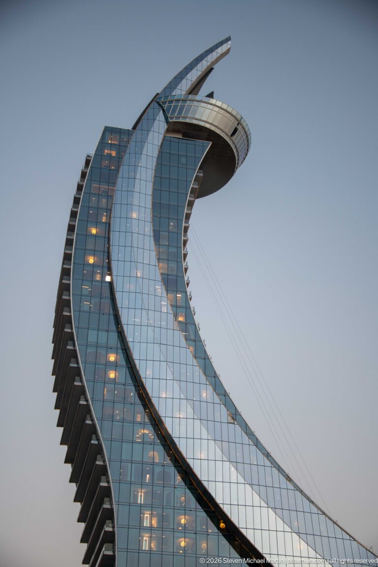 Curving glass tower rises to a broad cantilevered crown, with stepped balconies along one edge.