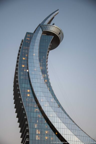 Curving glass tower rises to a broad cantilevered crown, with stepped balconies along one edge.
