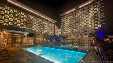 Turquoise swimming pool in a courtyard framed by two hotel wings with rows of illuminated square windows.