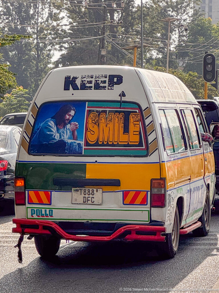 Rear of a brightly customized Arusha passenger minibus with religious artwork, a large SMILE panel, reflective markings, and painted trim.