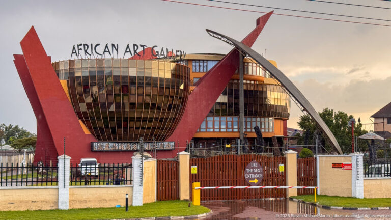 Roadside African Art Gallery building with curved vertical windows, large red sculptural supports, and a gated entrance.