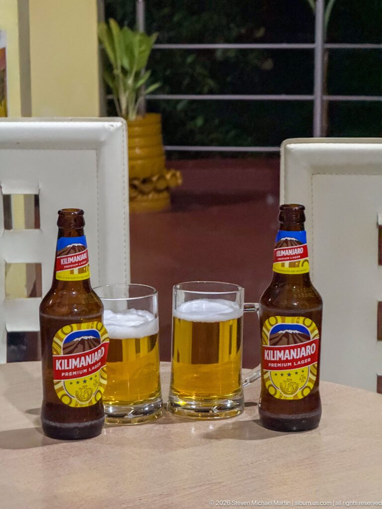 Two Kilimanjaro Premium Lager bottles beside two glasses of golden beer on an outdoor table.