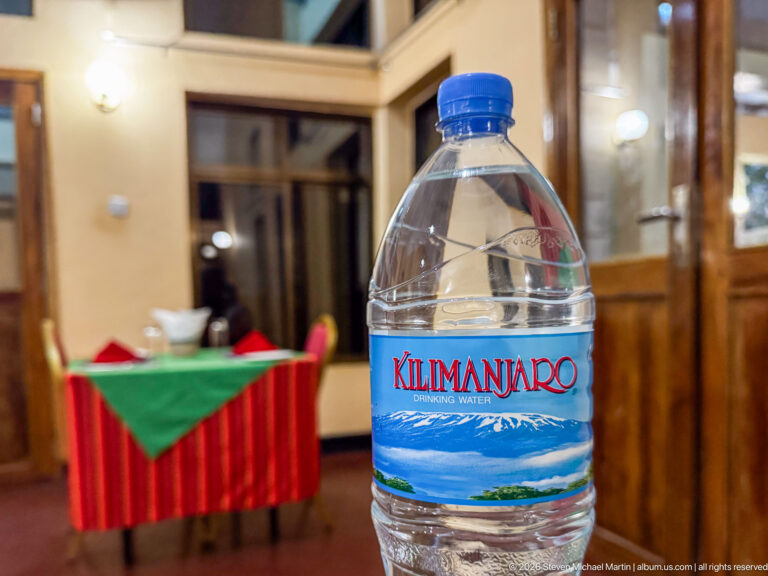 Kilimanjaro Drinking Water bottle in sharp focus with a red-and-green dressed dining table blurred behind it.