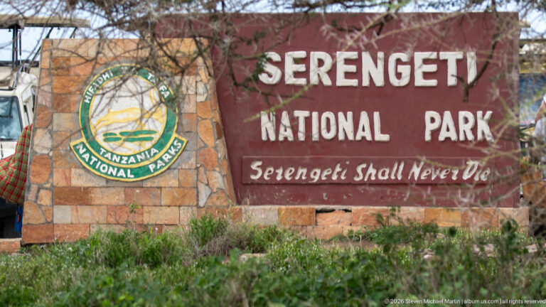 Stone Serengeti National Park sign with Tanzania National Parks emblem and the words “Serengeti Shall Never Die.”
