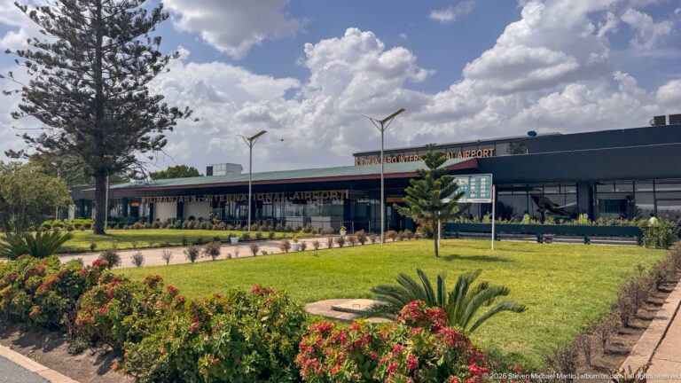 Kilimanjaro International Airport terminal behind landscaped lawn, flower beds and a broad paved approach.