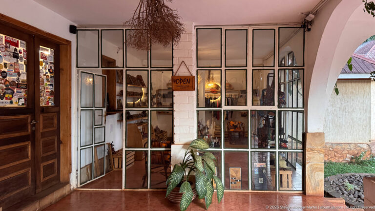 Glazed entrance to a small lodge shop with an OPEN sign, merchandise displays and potted plants.