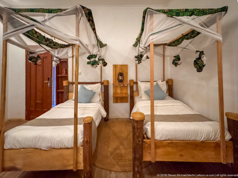 Two wooden single beds with white mosquito nets and green patterned trim in a simple guest room.