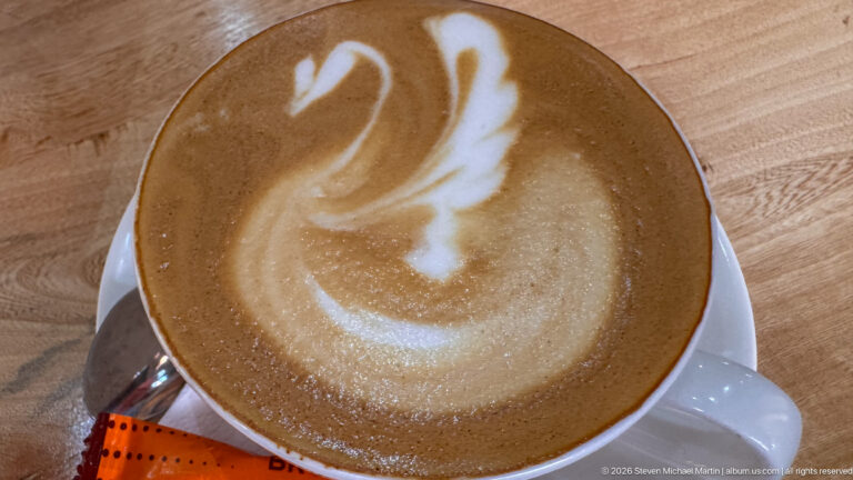 Overhead view of a latte in a white cup with swan-shaped foam art on a wooden table.