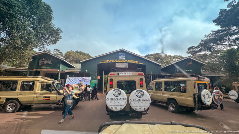 Safari vehicles and visitors clustered before the green-roofed Lodoare Gate entrance buildings at Ngorongoro Conservation Area.