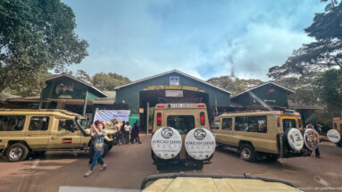 Safari vehicles and visitors clustered before the green-roofed Lodoare Gate entrance buildings at Ngorongoro Conservation Area.